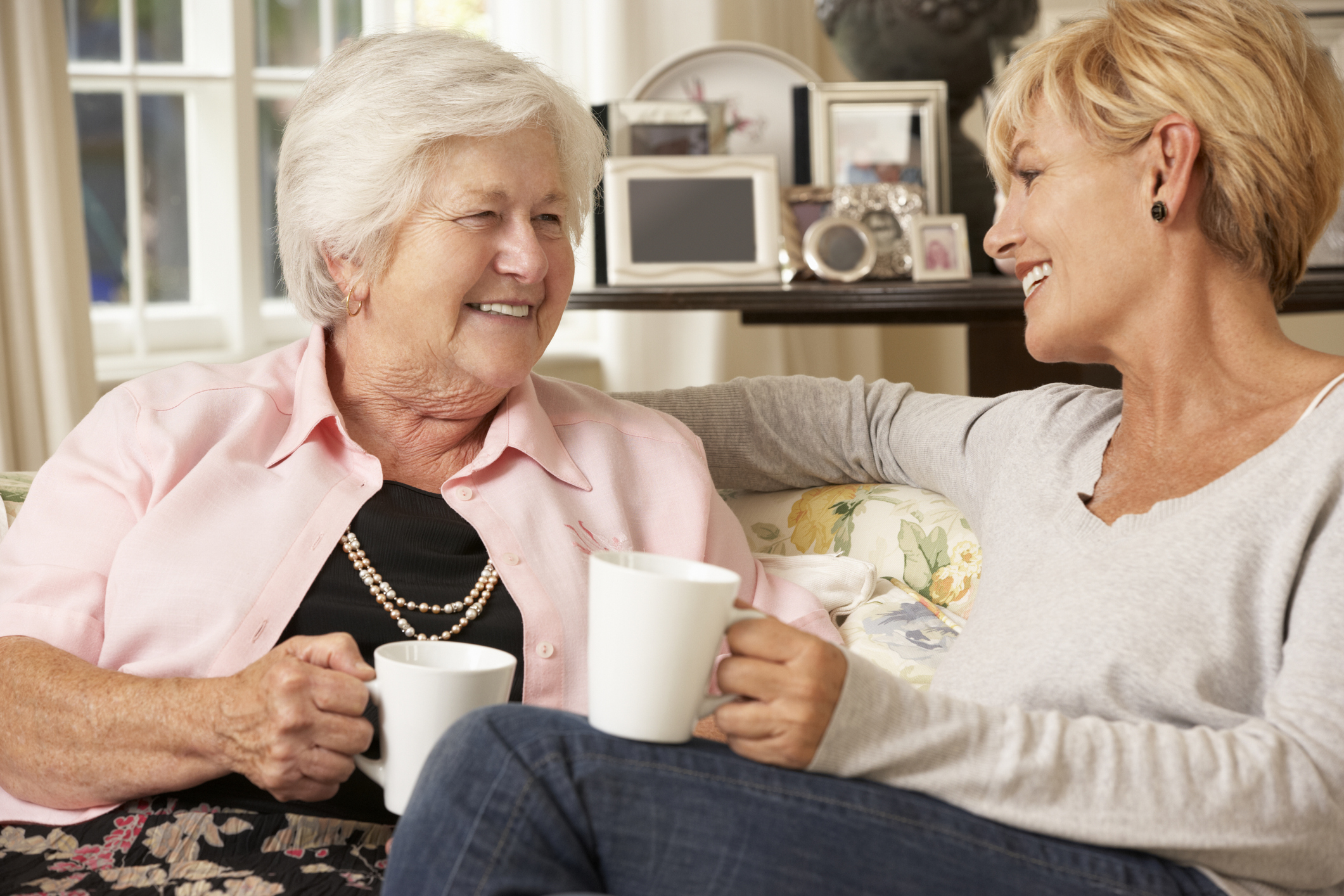 Adult daughter and senior mother sitting on a sofa smiling